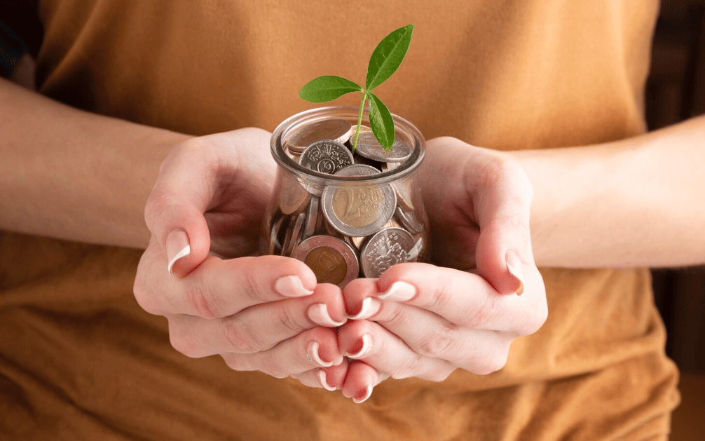 Manos sosteniendo tierra con una planta y monedas