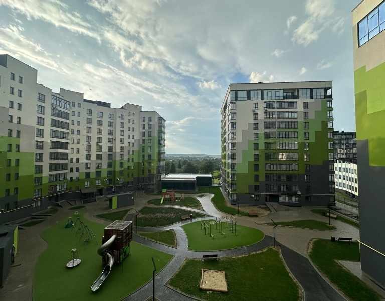Fotografía profesional de un complejo habitacional moderno con iluminación natural. Se observa a un joven ejecutivo frente a la fachada de un edificio nuevo. Estilo editorial de arquitectura.