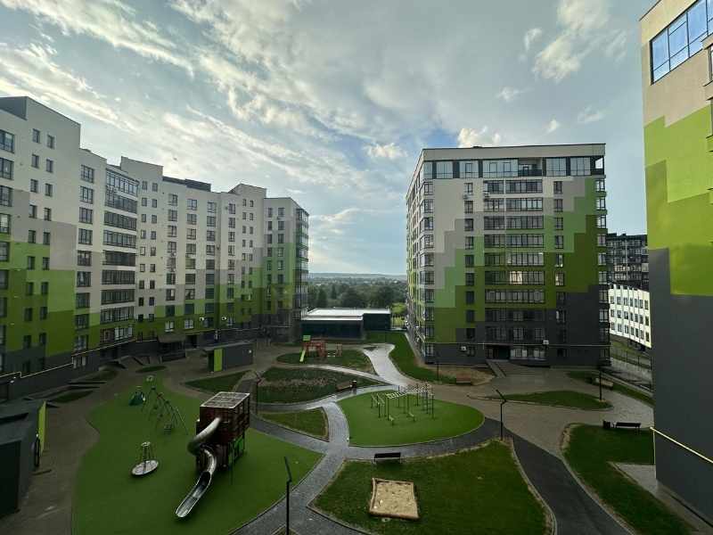 Fotografía profesional de un complejo habitacional moderno con iluminación natural. Se observa a un joven ejecutivo frente a la fachada de un edificio nuevo. Estilo editorial de arquitectura.