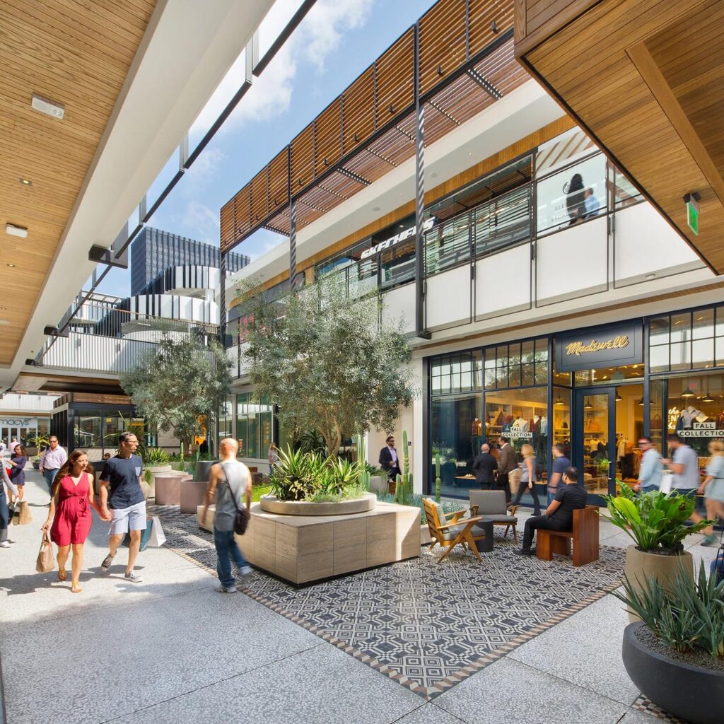 Plaza comercial moderna con tiendas, restaurantes y áreas peatonales donde las personas realizan compras y conviven.